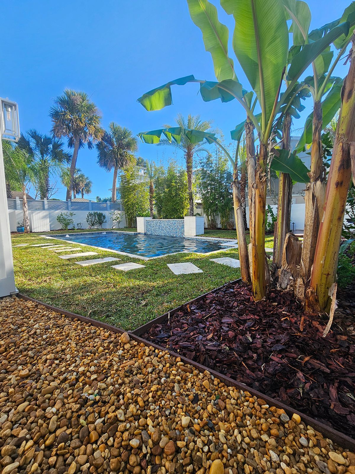 A lush green garden with a swimming pool and palm trees.