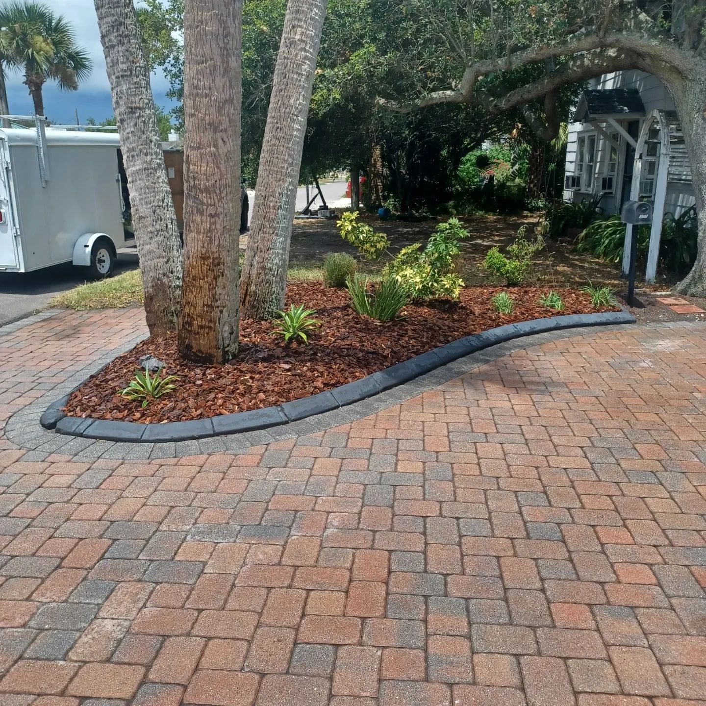 A brick driveway with a white trailer parked in the background.