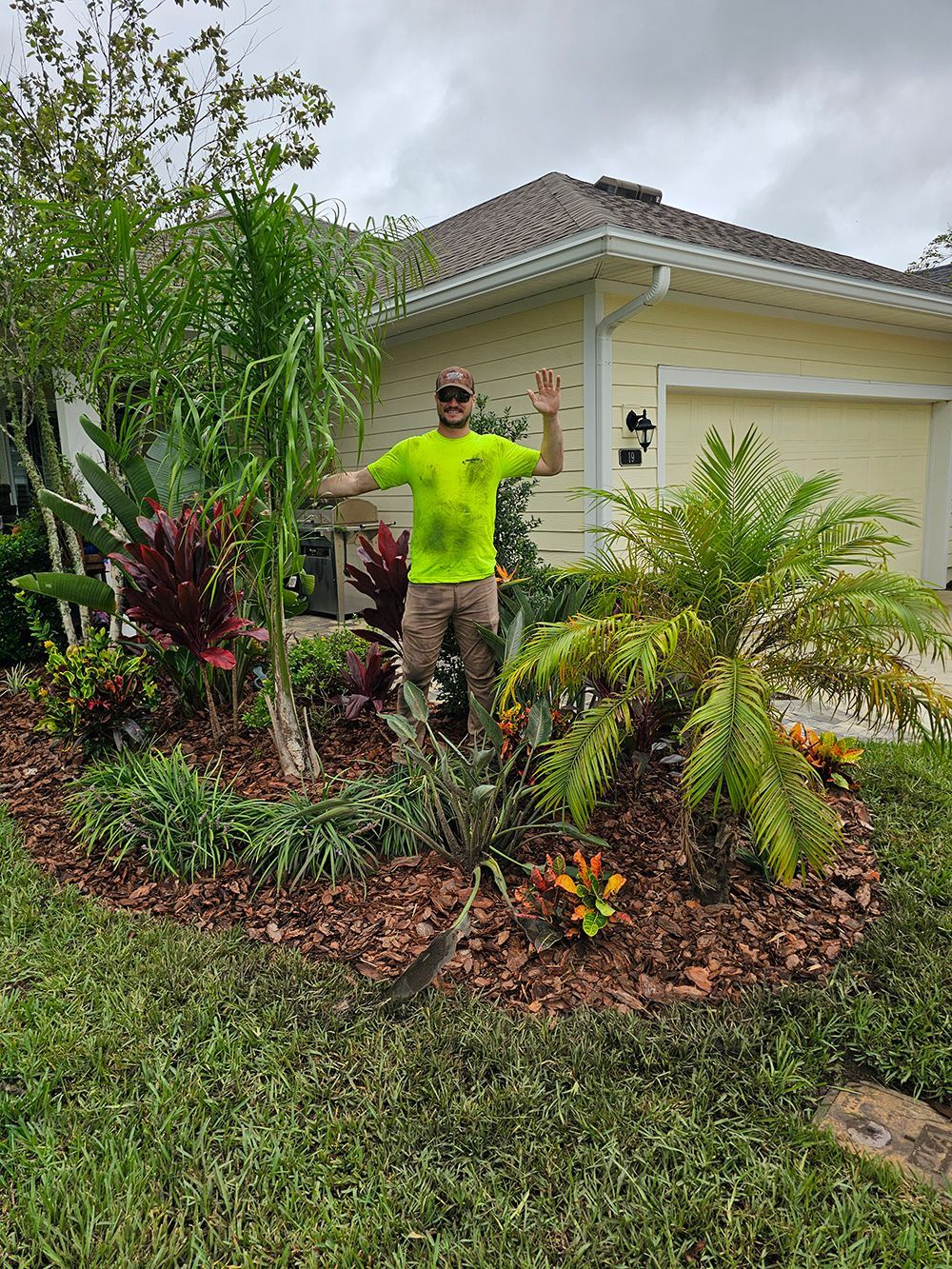 A man in a neon green shirt is standing in a garden in front of a house.