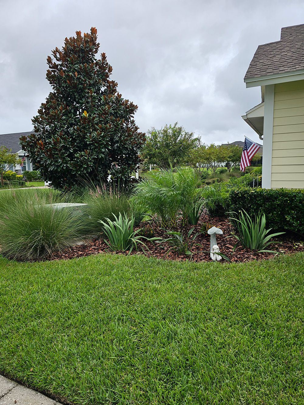 A lush green lawn in front of a house with a flag in the background.