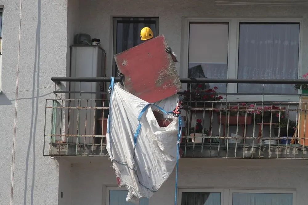 A Person Wearing a Yellow Hard Hat Is Standing on A Balcony Holding a Large Bag — Lifestyle Demolition In Mullumbimby, NSW