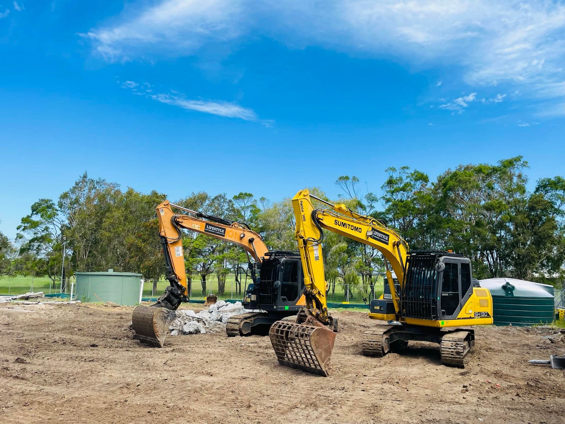 Two yellow and orange excavators on a construction site under a bright blue sky. — Lifestyle Demolition In Lismore, NSW