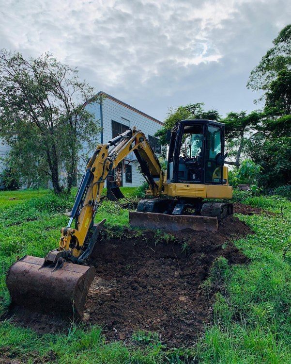Yellow Excavator Digging in a Grassy Area Near a White Building — Lifestyle Demolition In Byron Bay, NSW