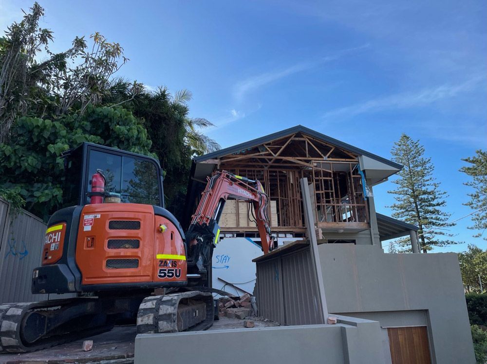 A Yellow Excavator Is Demolishing a House — Lifestyle Demolition In Bangalow, NSW