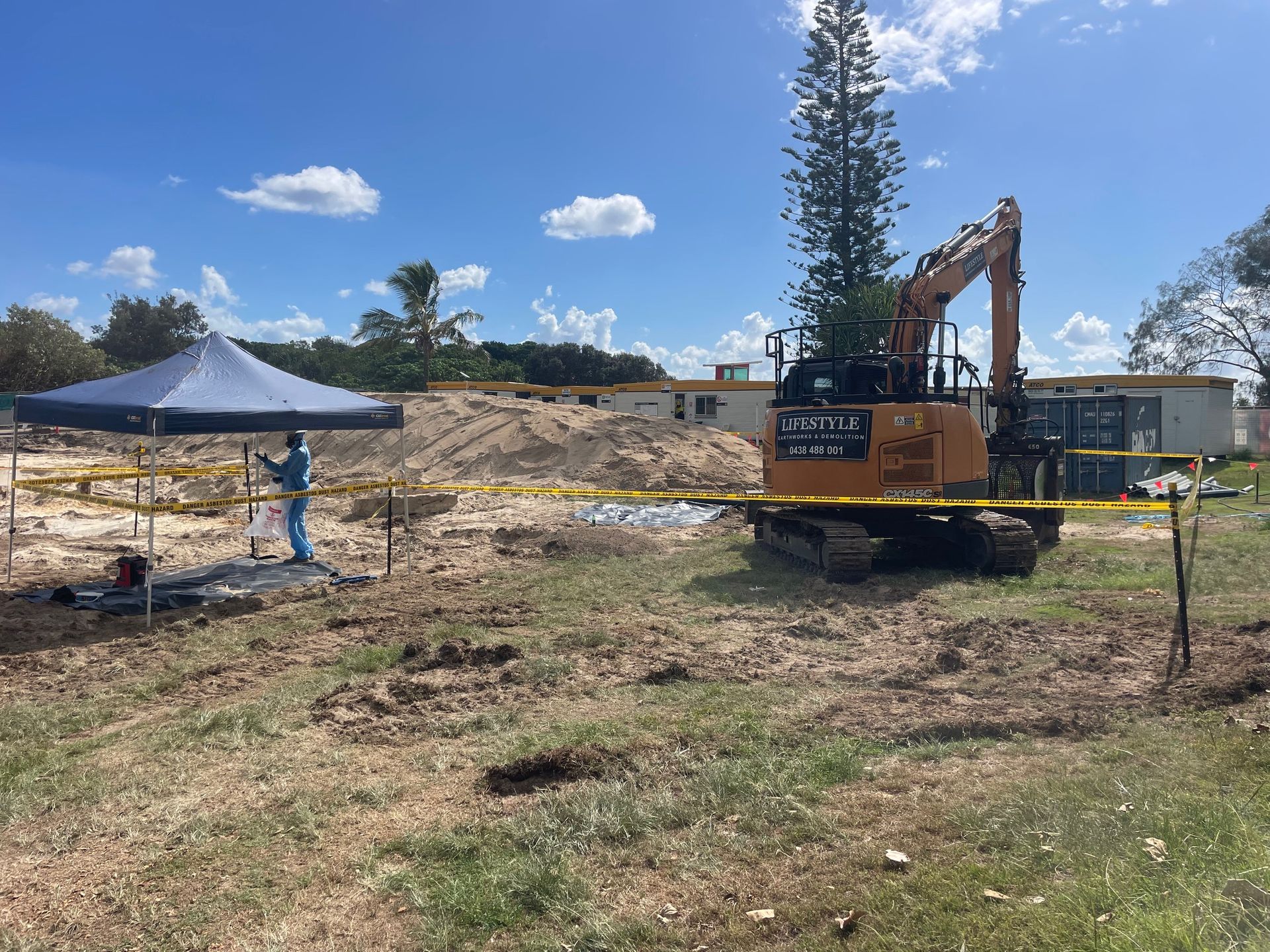 An Excavator Digging Into Reddish-Brown Earth Next To A White Dump Truck — Lifestyle Demolition In Kingscliff, NSW