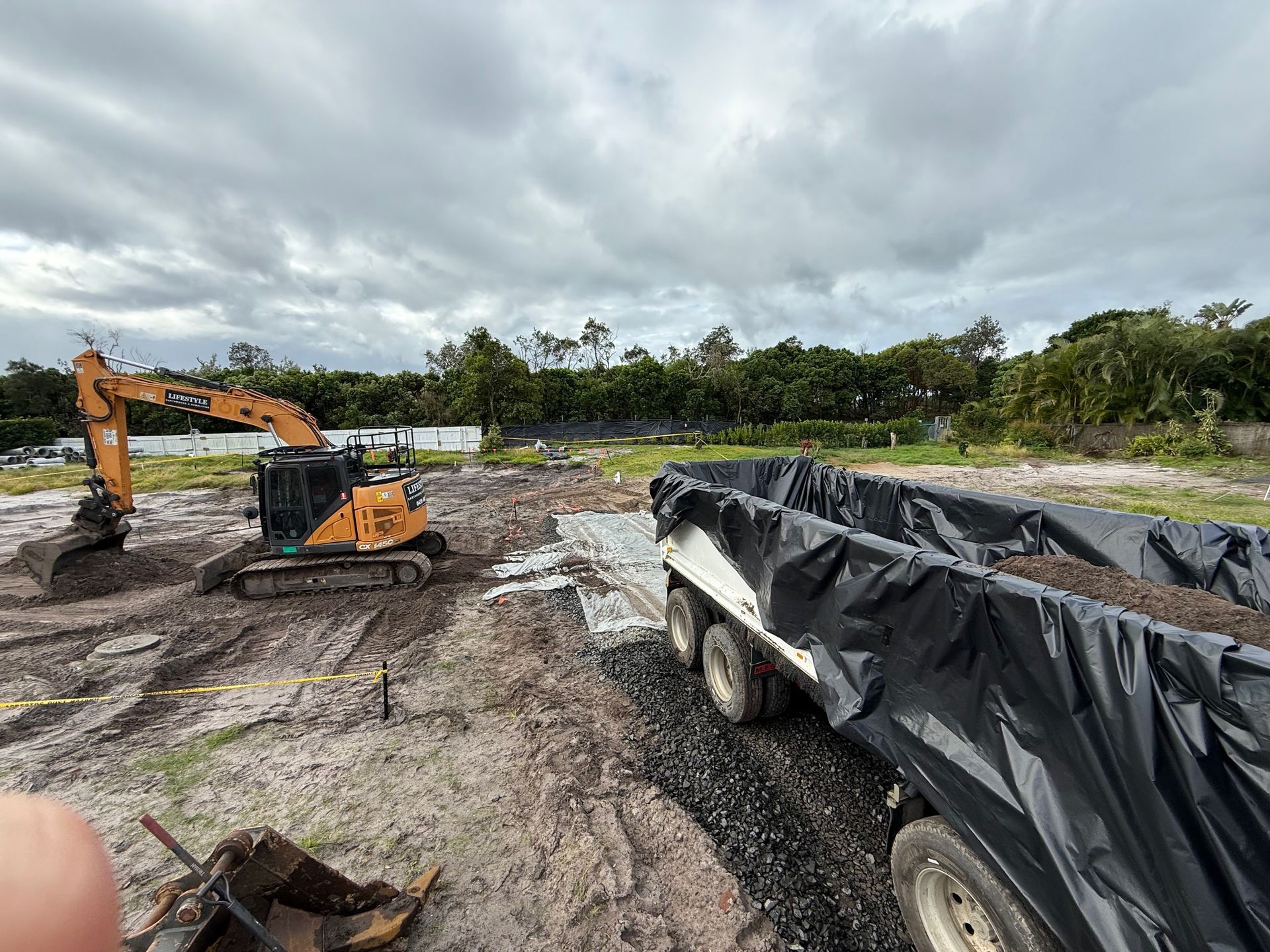 A Yellow Excavator Removing Tree Roots From A Muddy Yard — Lifestyle Demolition In Kingscliff, NSW
