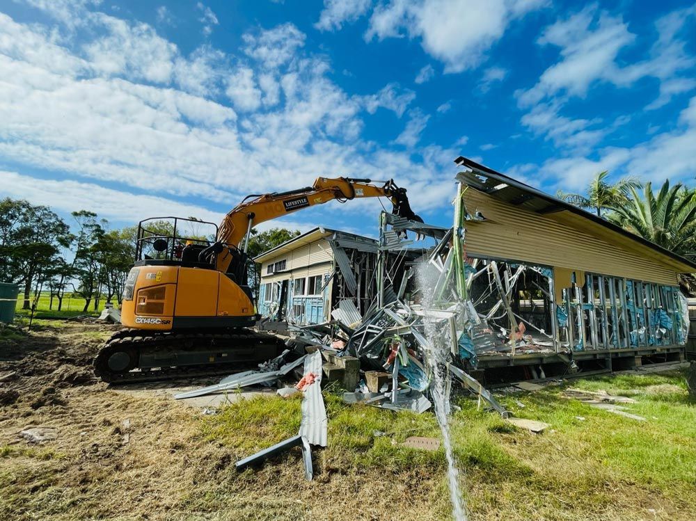 An Excavator Is Demolishing a House in A Field — Lifestyle Demolition In Tweed Heads, NSW