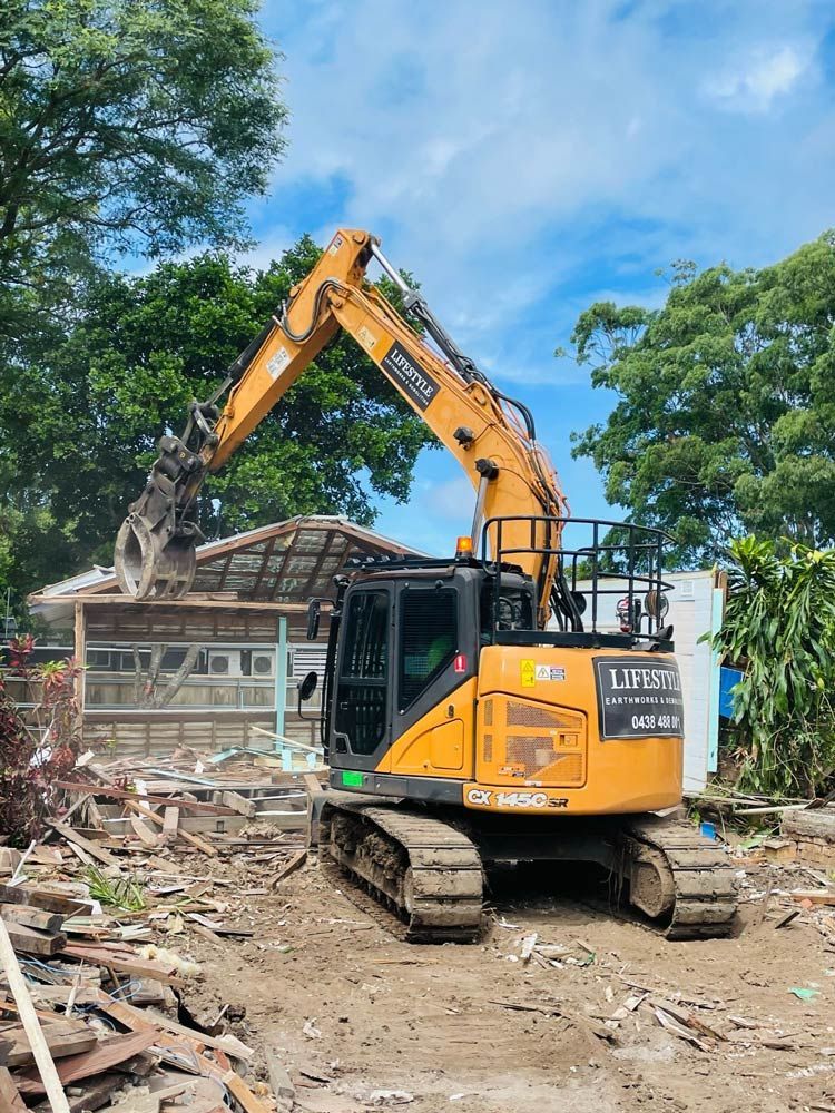 A Yellow Excavator Is Demolishing a Concrete Building — Lifestyle Demolition In Tweed Heads, NSW
