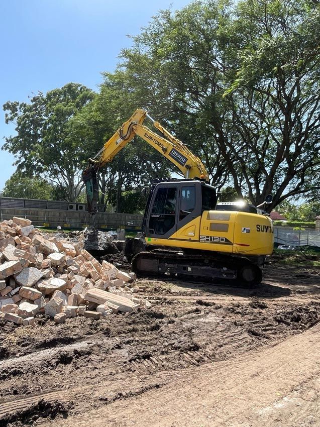 Yellow Excavator Demolishing Debris on A Muddy Construction Site — Lifestyle Demolition in Kingscliff, NSW