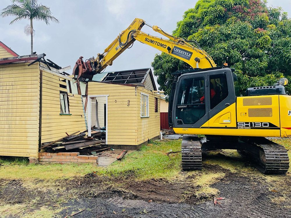 A Yellow Excavator Is Loading Dirt Into a Dump Truck at A Construction Site — Lifestyle Demolition In Brunswick Heads, NSW