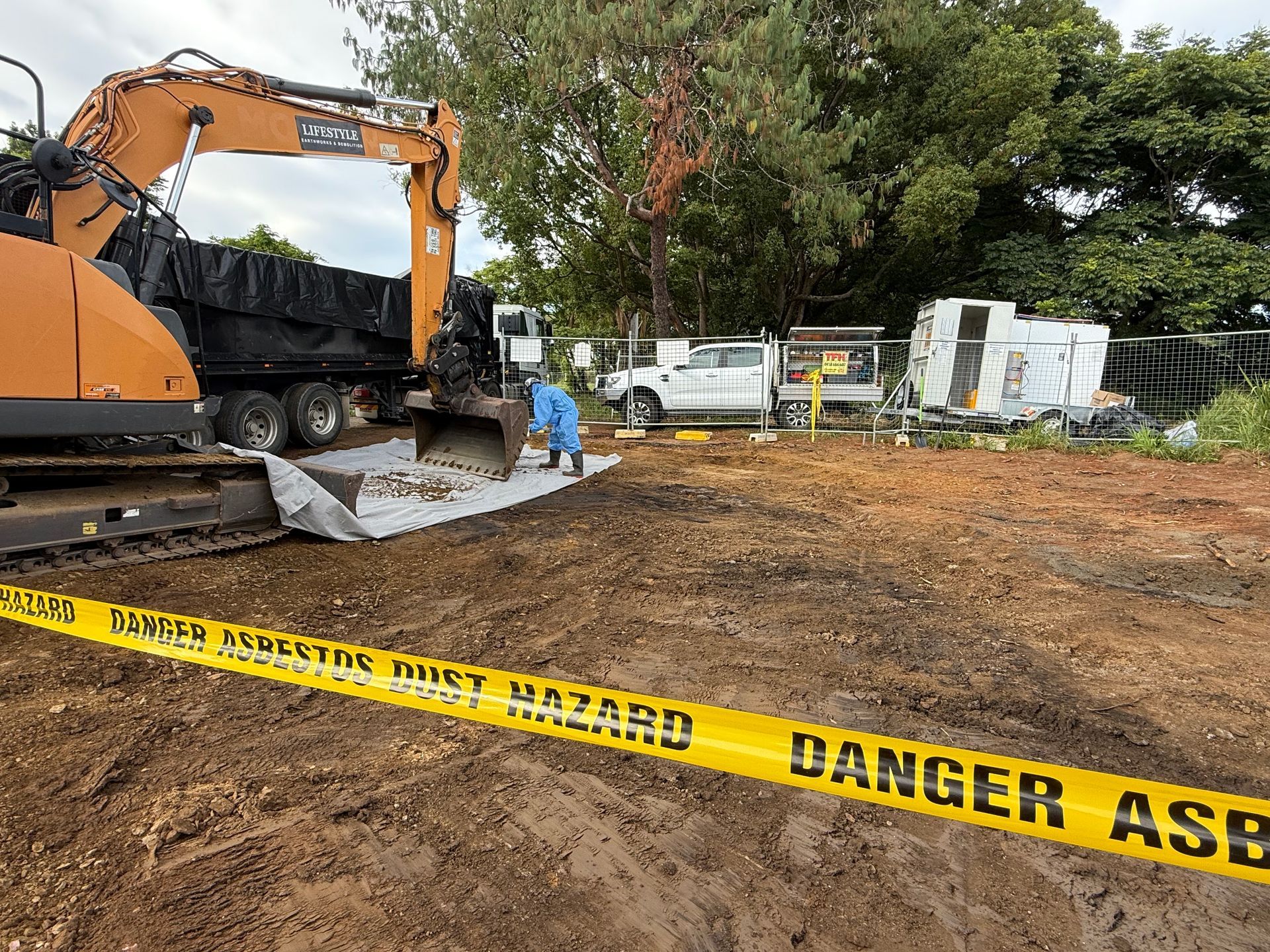 Construction site with excavator, workers, and yellow danger tape over muddy ground — Lifestyle Demolition In Ballina, NSW