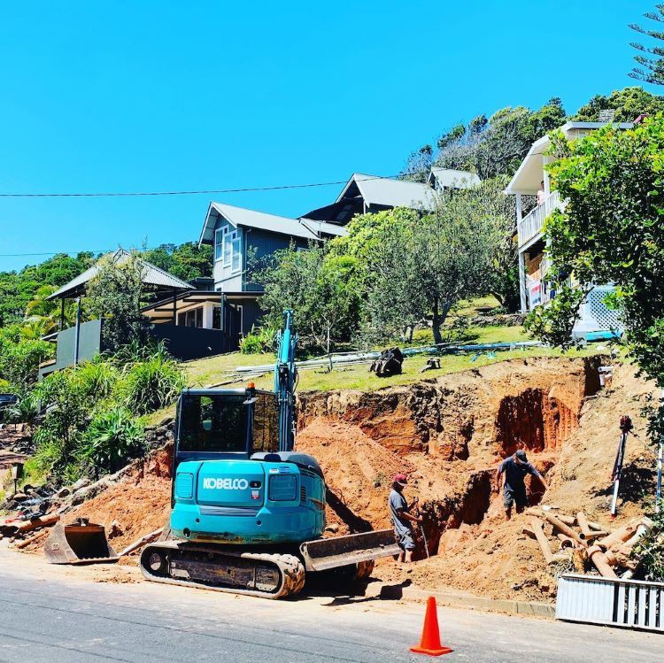 Blue Excavator on a Road Near a Hillside Construction Site, Houses on the Hill — Lifestyle Demolition In Byron Bay, NSW