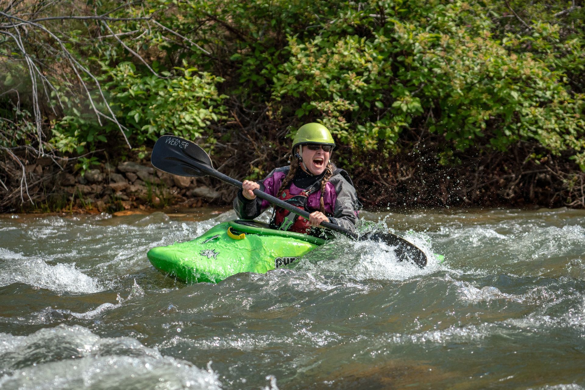 A man is paddling a green kayak down a river.