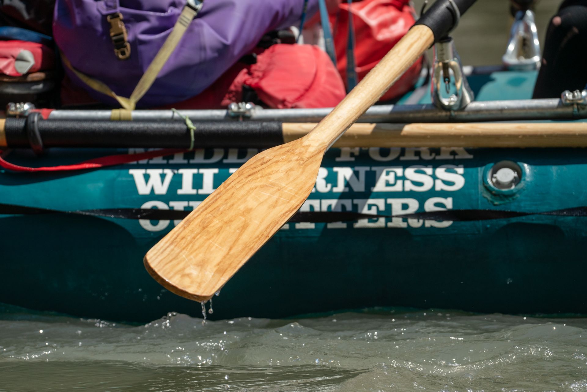 A wooden paddle is being used in a canoe that says witness on the side