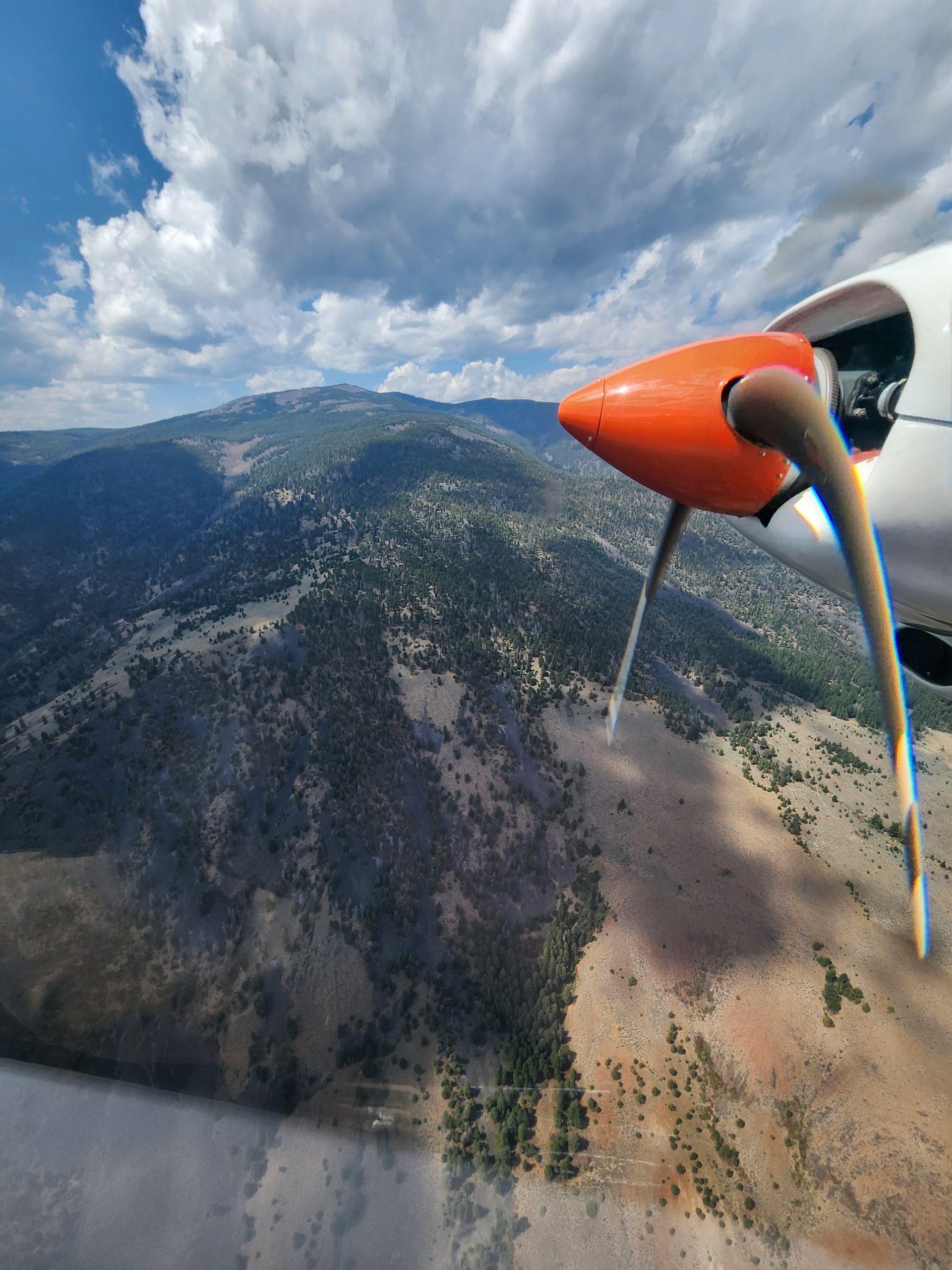 A plane is flying over a valley with mountains in the background