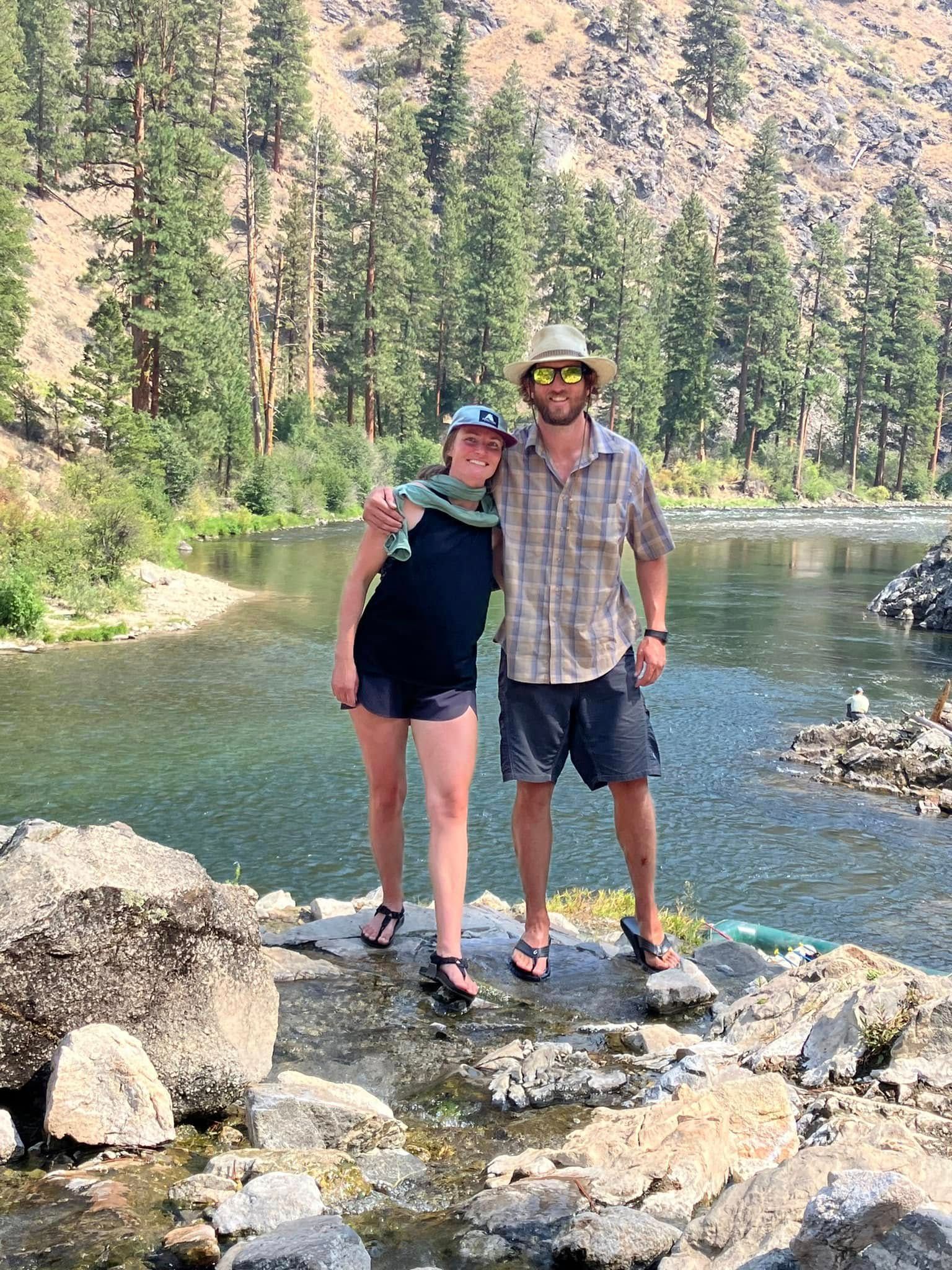A man and a woman are posing for a picture in front of a lake.