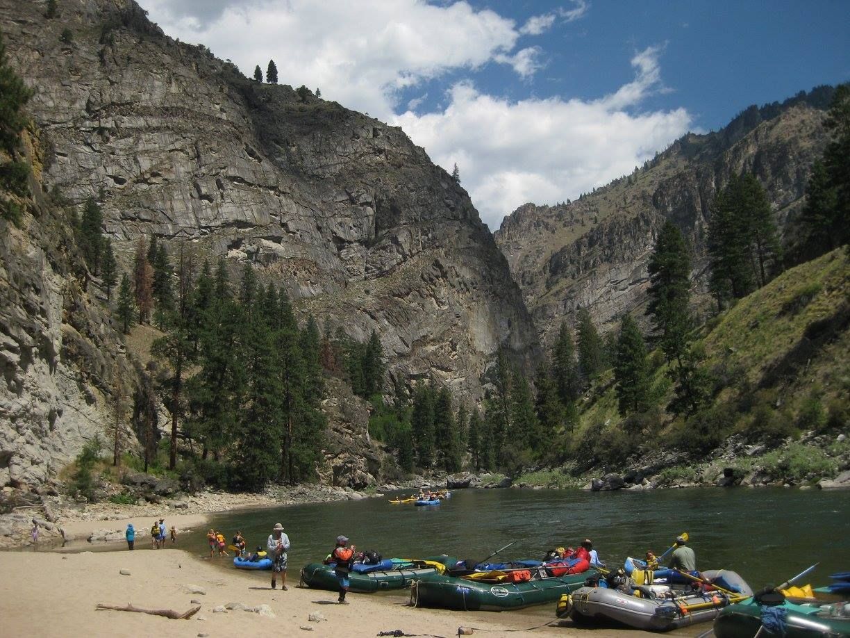 A group of people are rafting down a river with mountains in the background