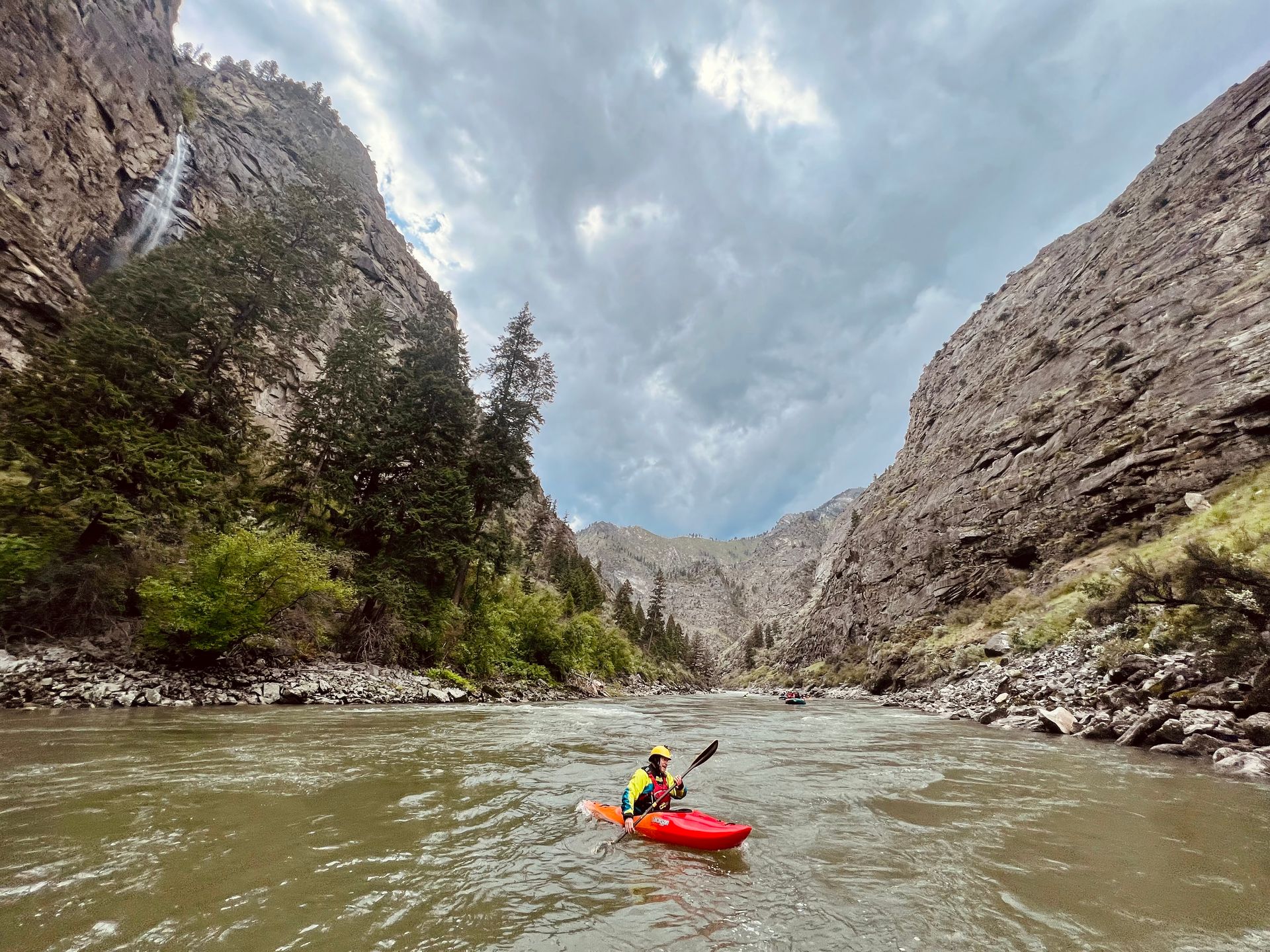 A person is paddling a red kayak down a river.