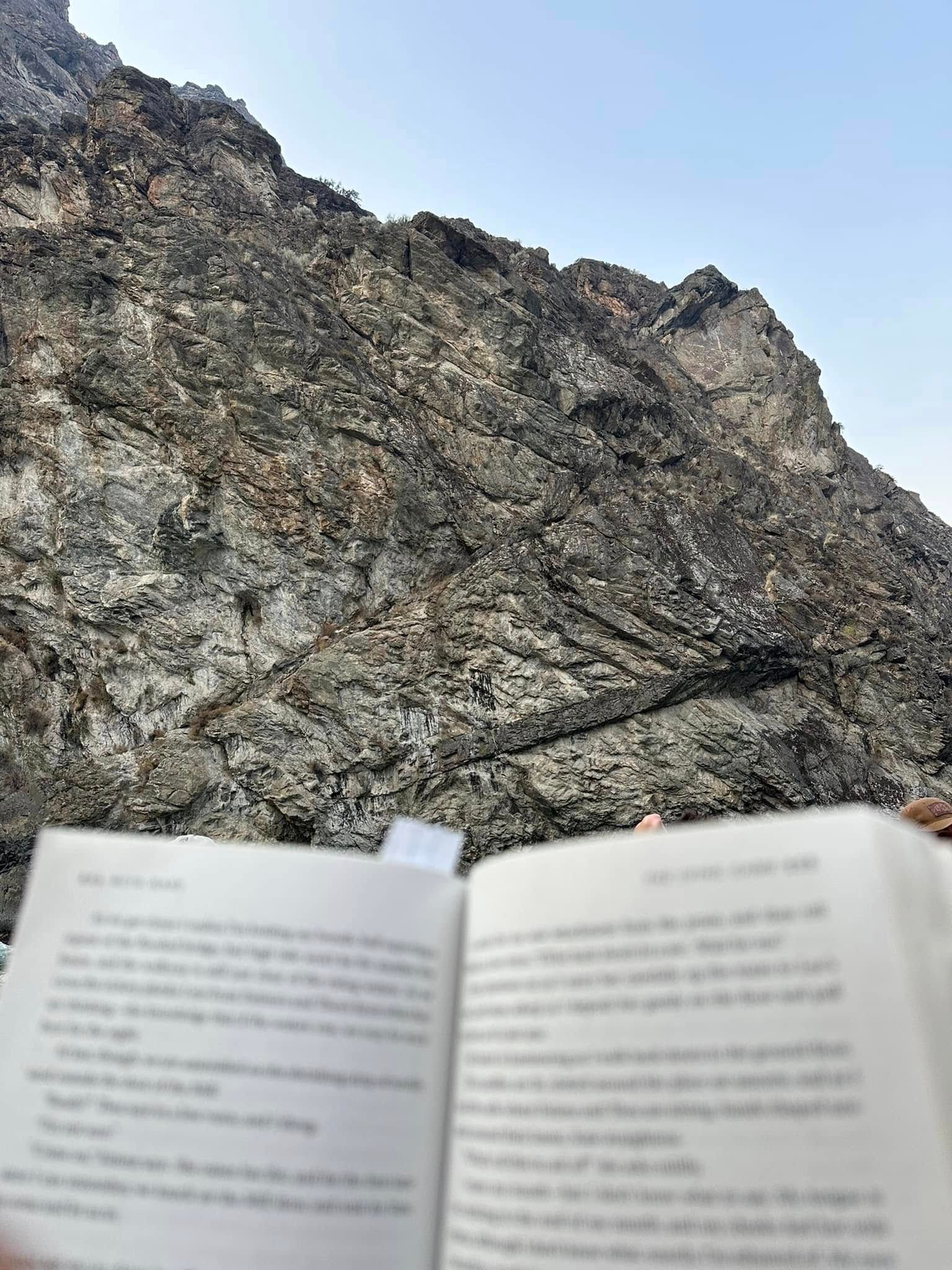 A person is holding a book in front of a mountain.