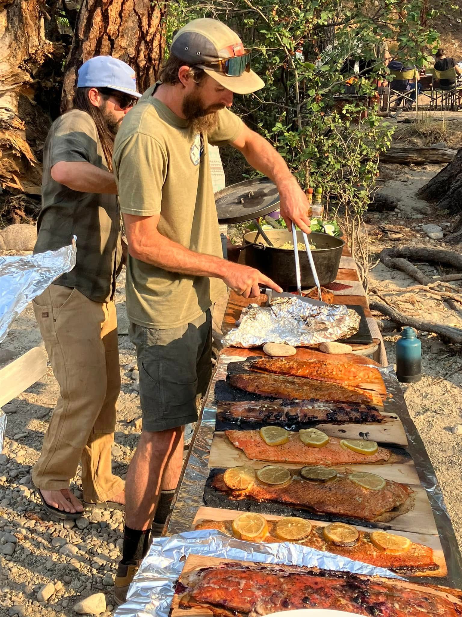 Two men are standing at a long table cooking food.