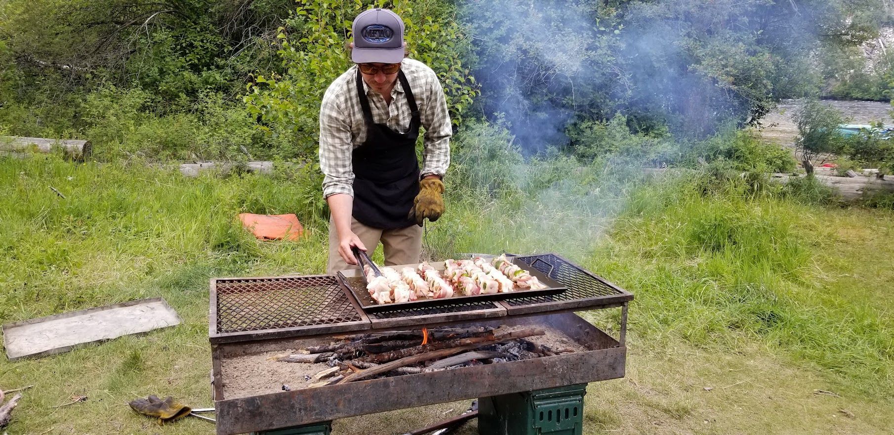 A man is cooking food on a grill in the grass.