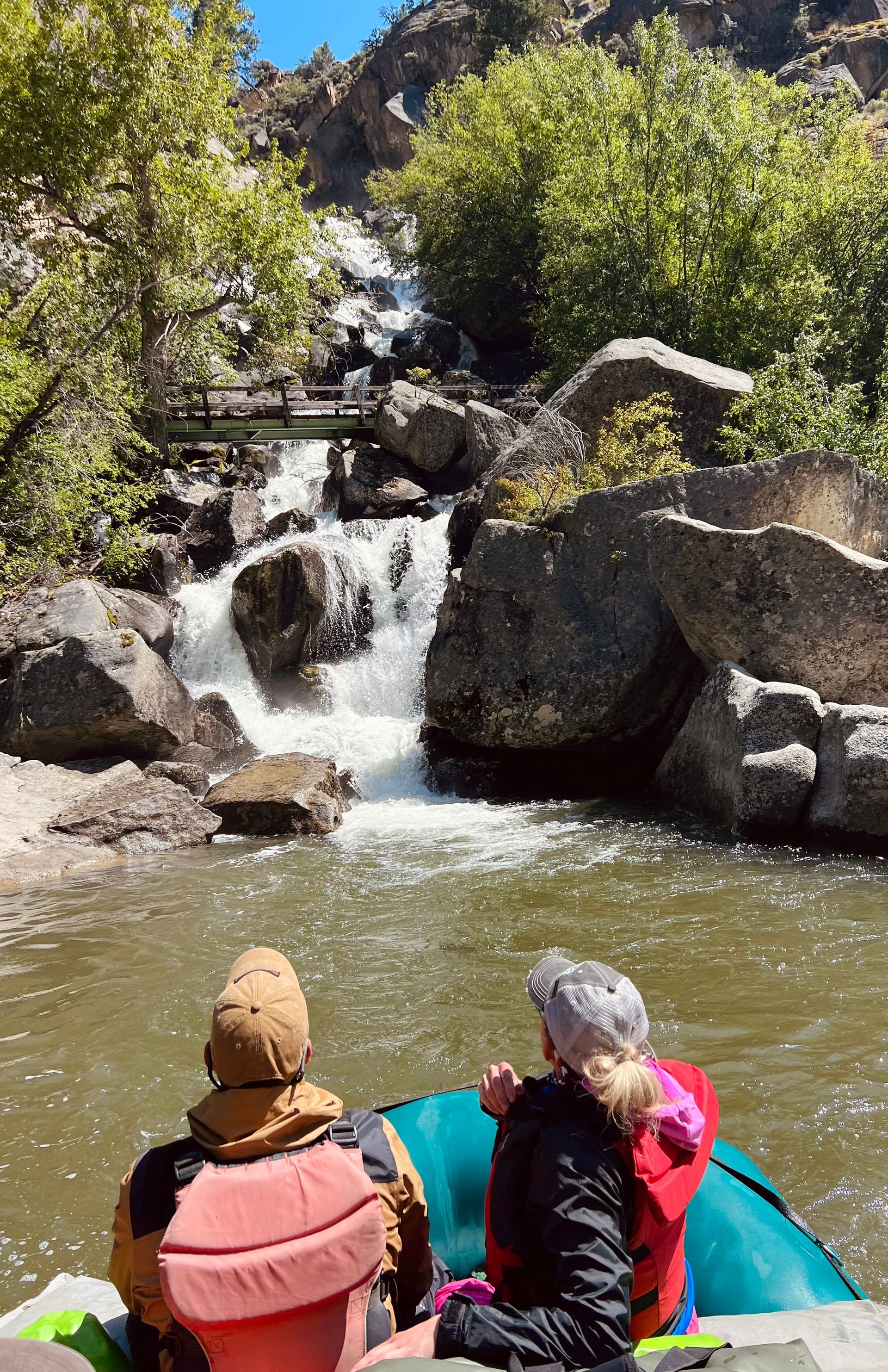 Two people are sitting in a raft looking at a waterfall.