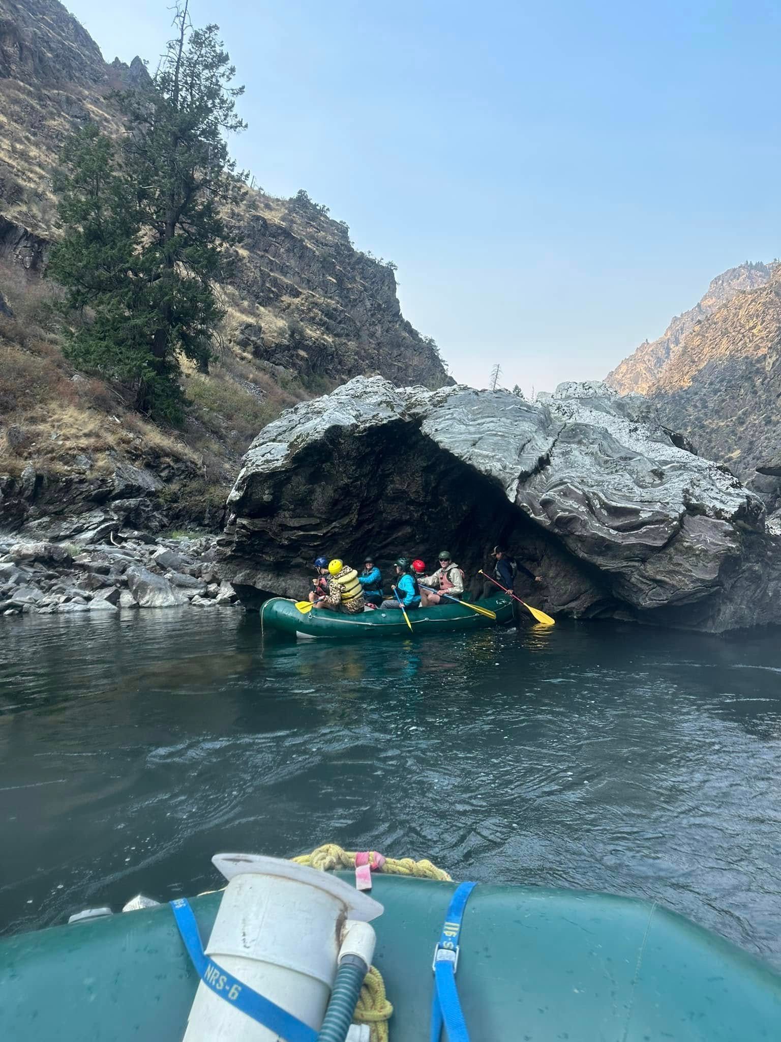 A group of people are rafting down a river near a cave.