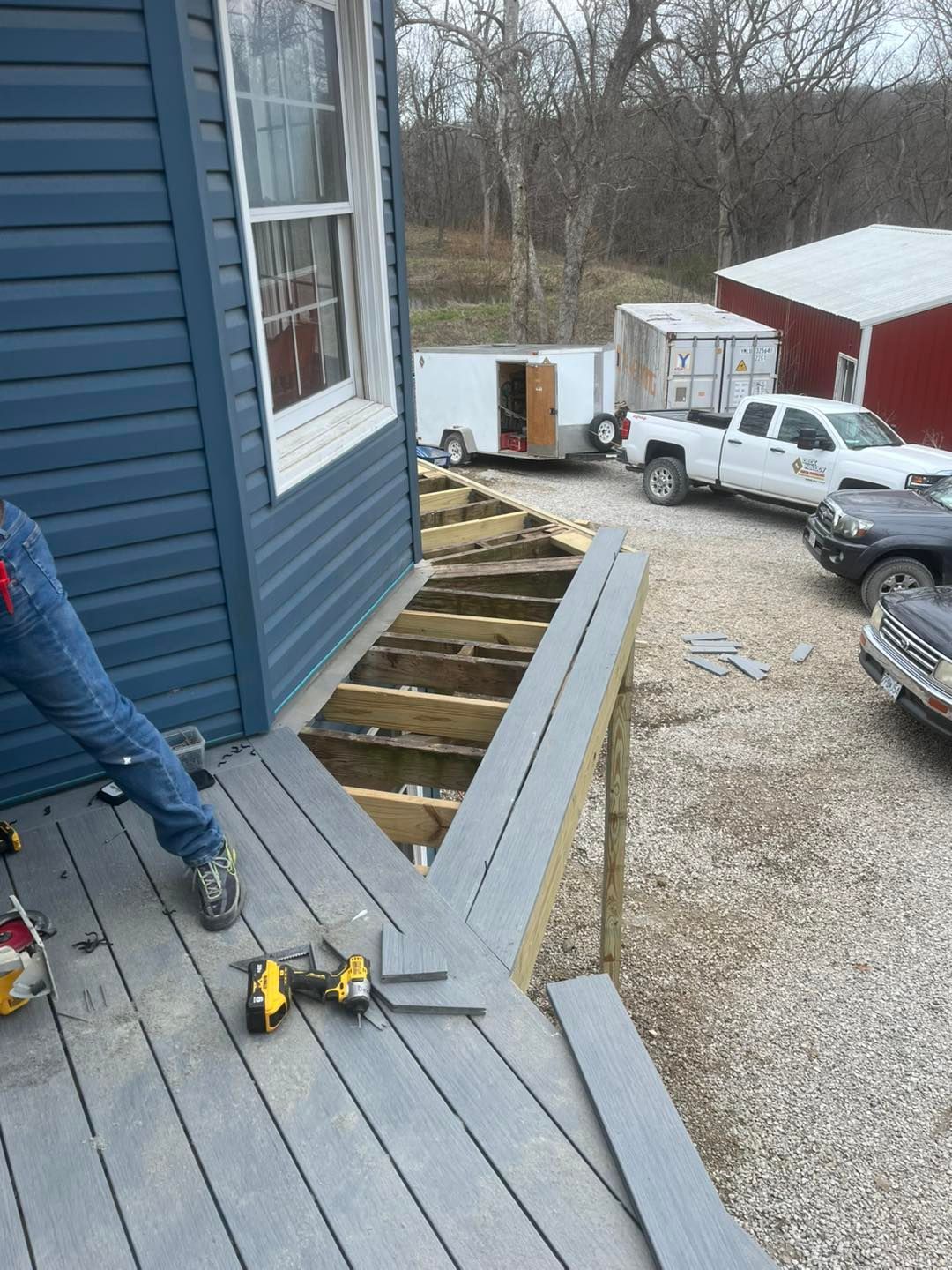 Construction of a gray composite deck next to a blue house. A person in jeans 
