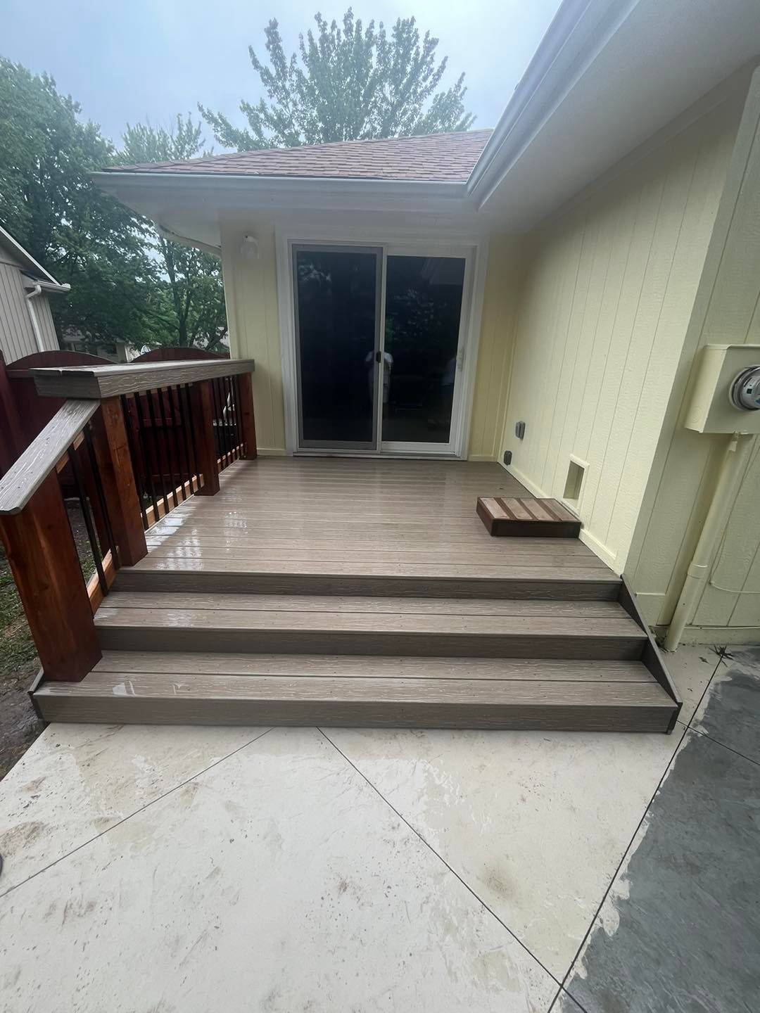 A wooden deck with stairs leading to a sliding glass door. The deck and steps are gray, and the railing is brown.