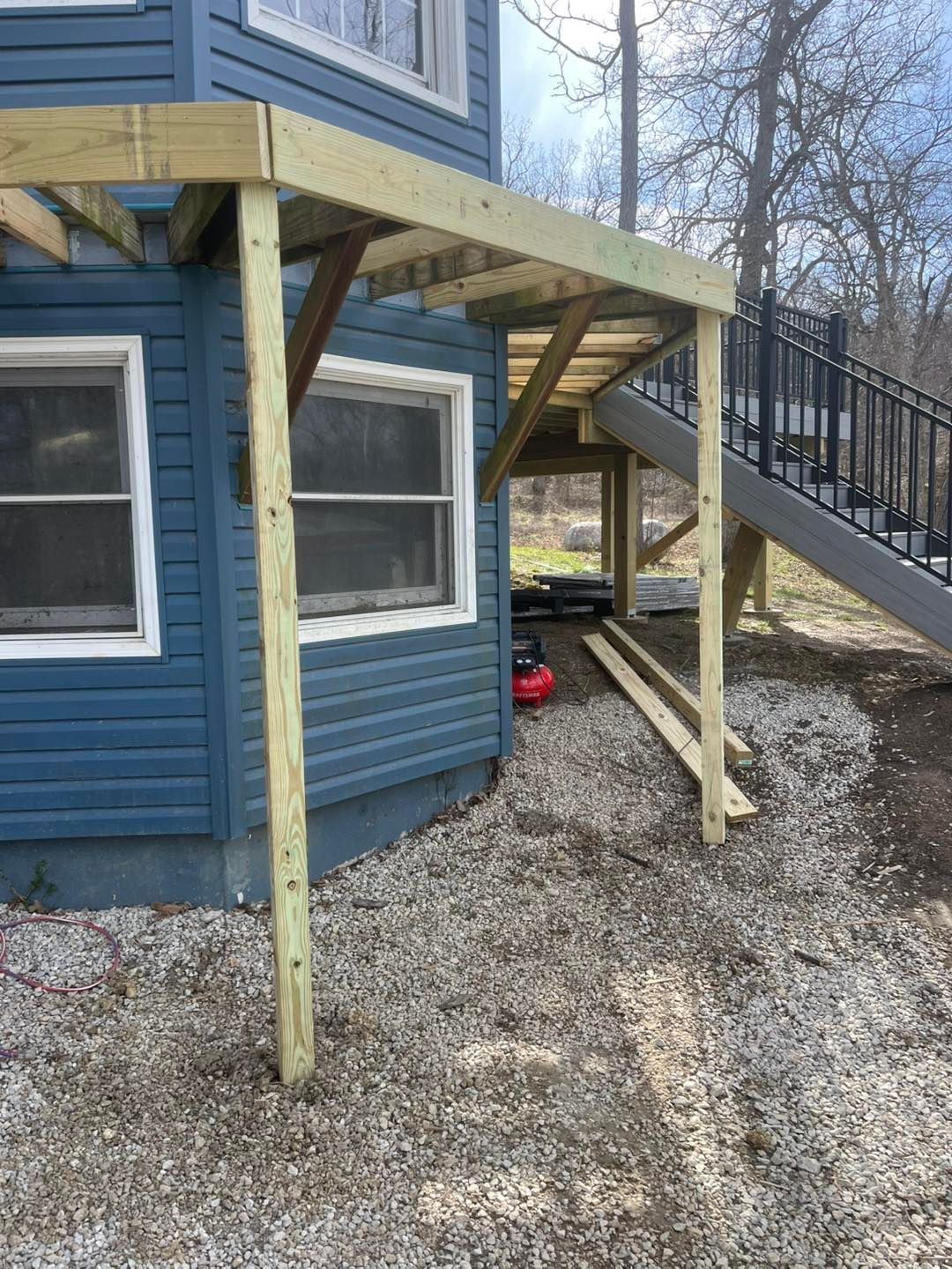 A wooden deck addition with support beams next to a blue house. A set of stairs and a slide are visible.