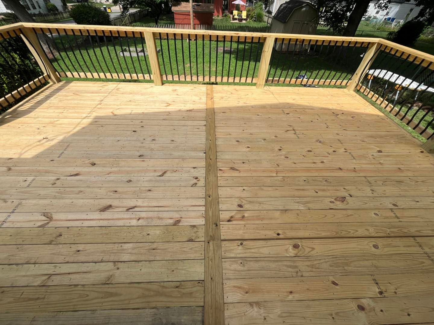 Wooden deck with black metal railings overlooking a green lawn.
