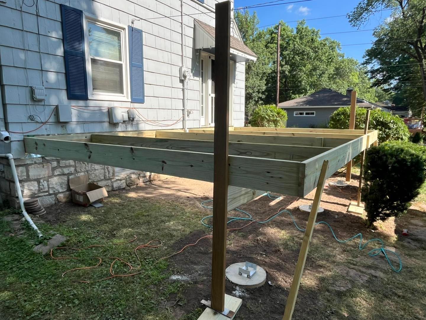 A partially built deck attached to a light-colored house with a front yard, supported by wooden posts.