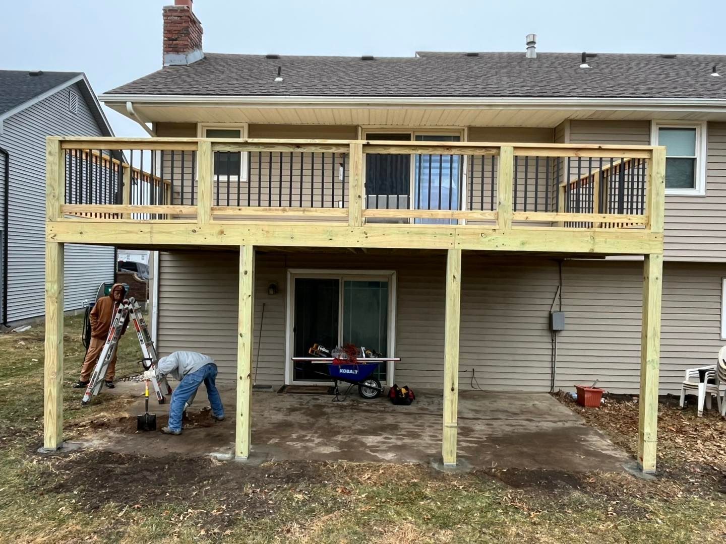Construction of a two-level wooden deck attached to a beige house; a worker 
