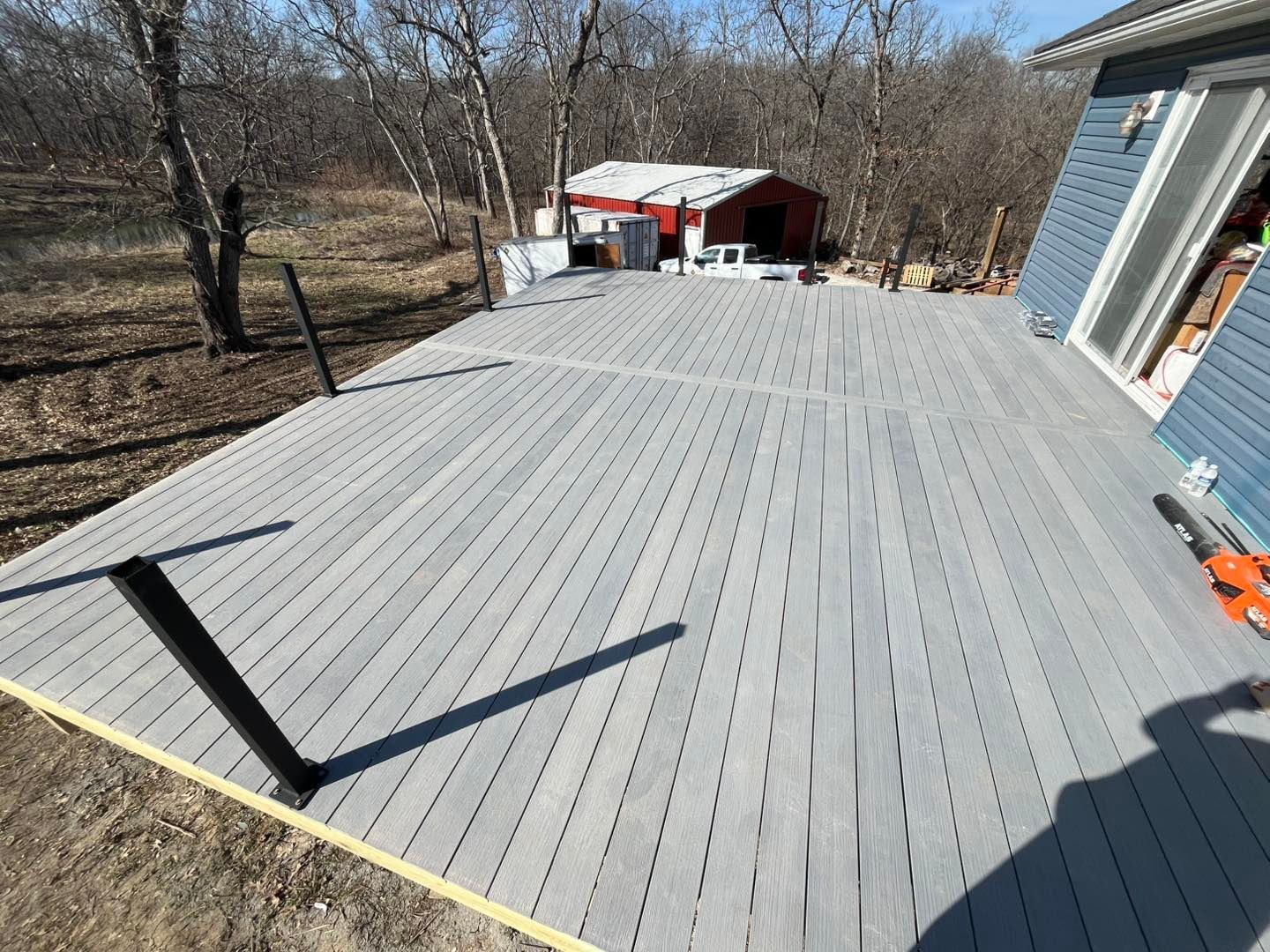 Large, grey composite deck extending from a blue house, with a small red shed in the background.