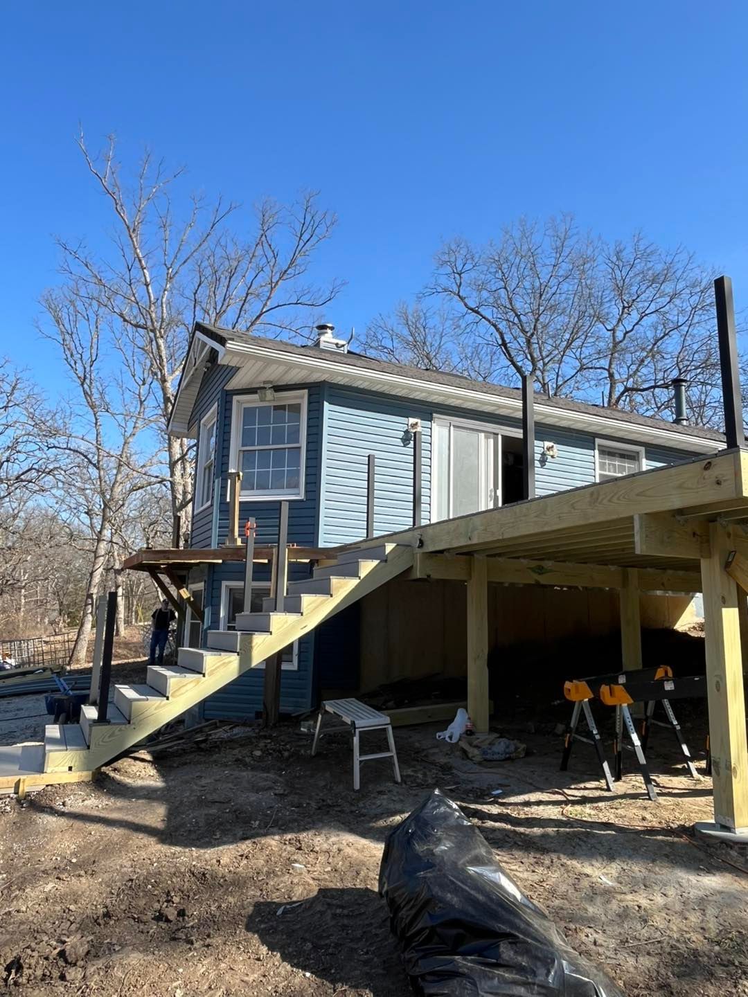 A blue house with a deck under construction. A staircase leads up to a sliding glass door. The sky is clear.