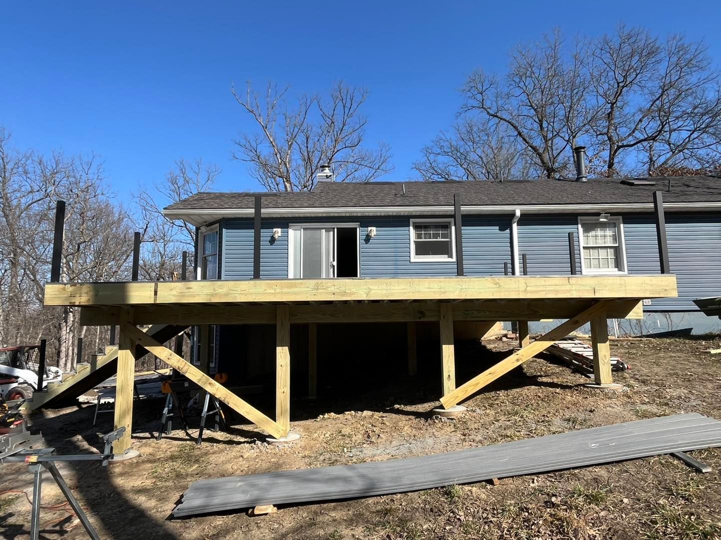 A newly built wooden deck with black railings attached to a blue house, set outside in a yard.