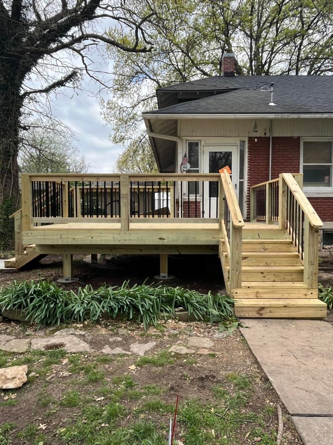 New wooden deck with stairs leading to the front door of a red-sided house, built above low landscaping.
