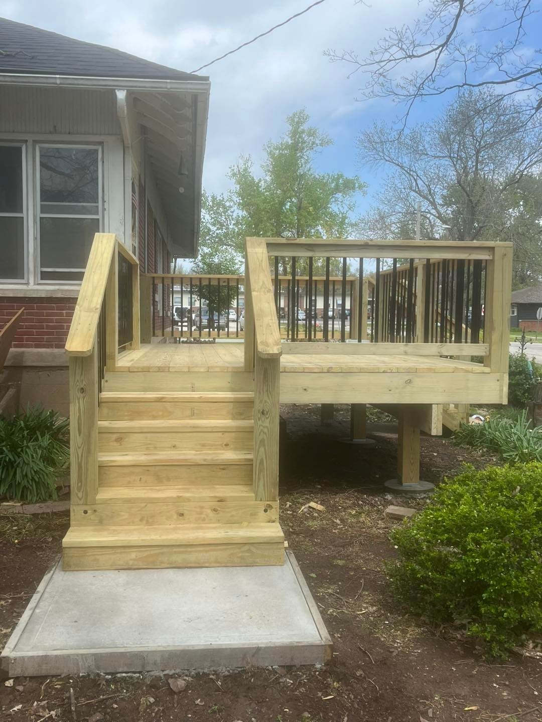 Newly built wooden deck and stairs attached to a house, with a concrete slab at the base.