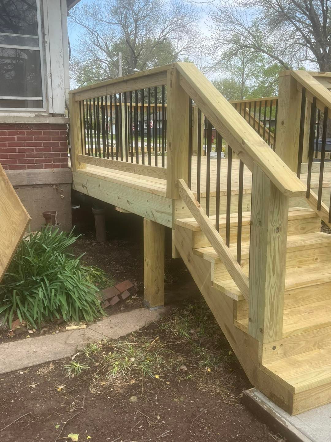 Newly constructed wooden deck with stairs and black metal railings next to a 