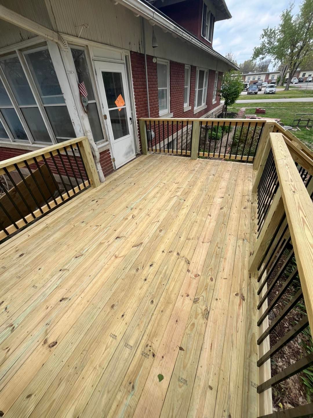 Wooden deck attached to a brick house, featuring black railings, new light-colored wood, and a glass-paned door.