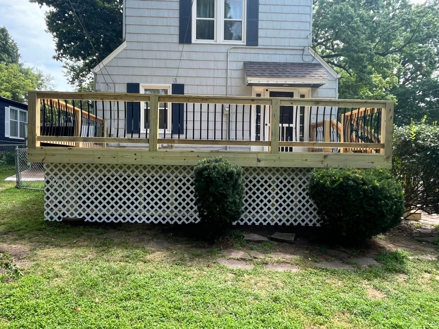 Newly constructed wooden deck with white lattice skirting, connected to a gray house with black shutters.