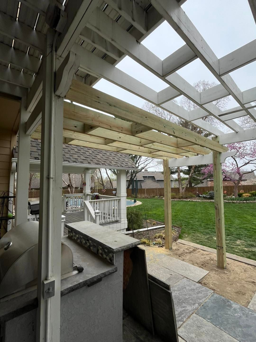 A partially constructed pergola over an outdoor kitchen and patio. White and 