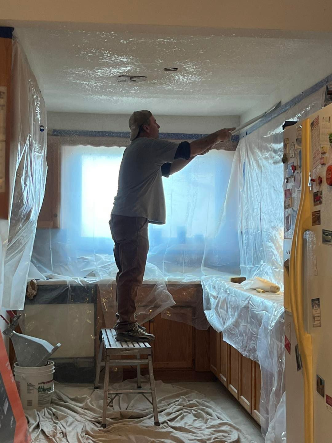 A person on a step stool is working on a kitchen ceiling, applying something with 