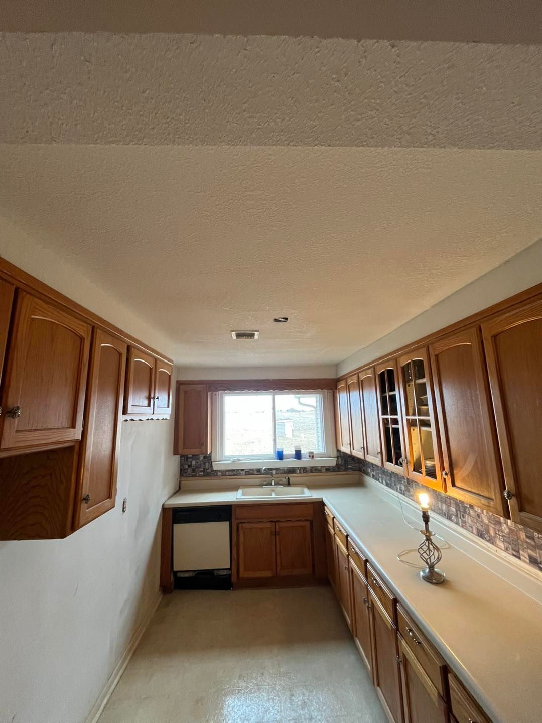 Kitchen with wood cabinets, white countertops, and a window above the 