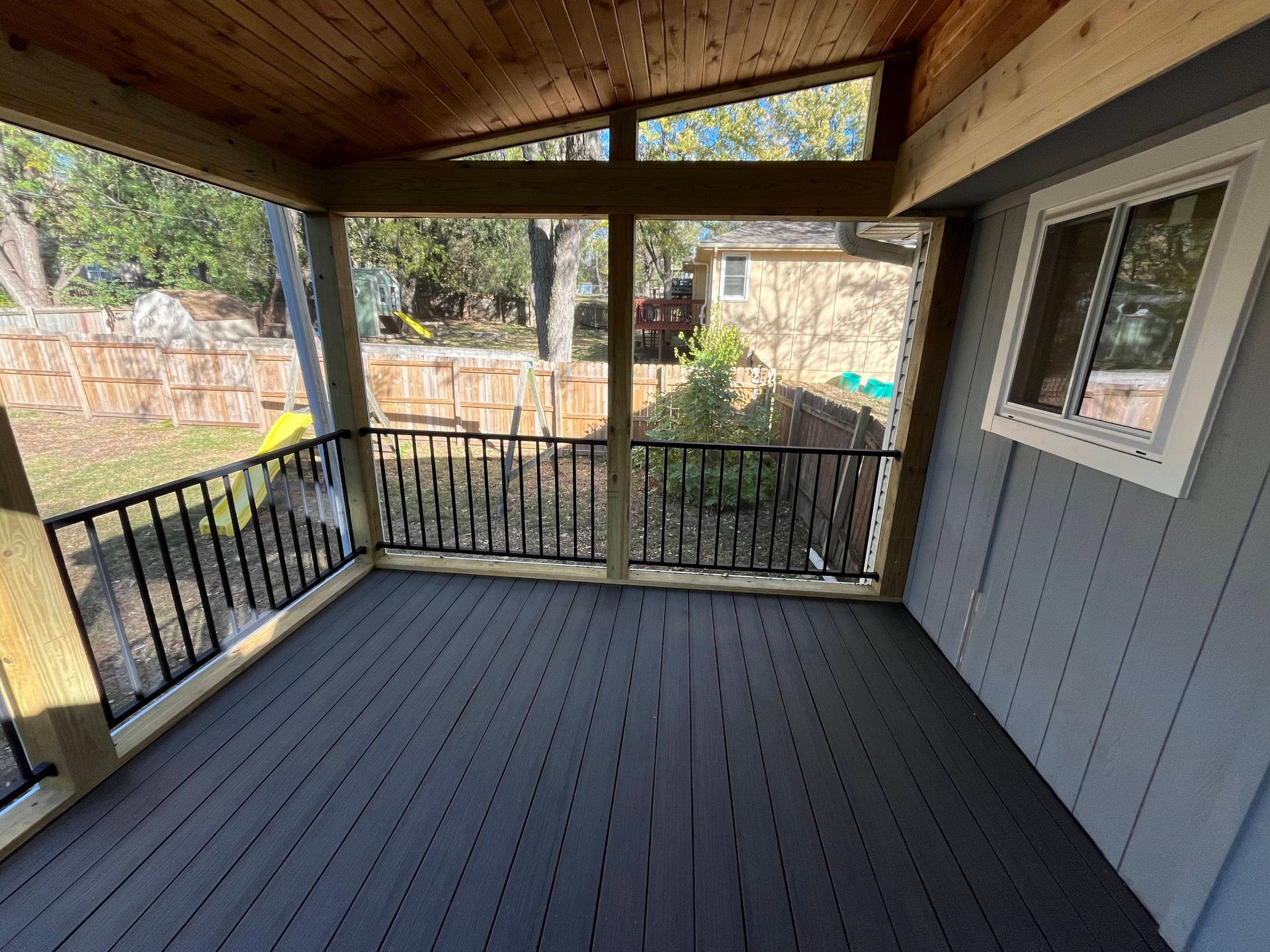 Covered porch with black railings, dark gray flooring, and a view of a backyard.