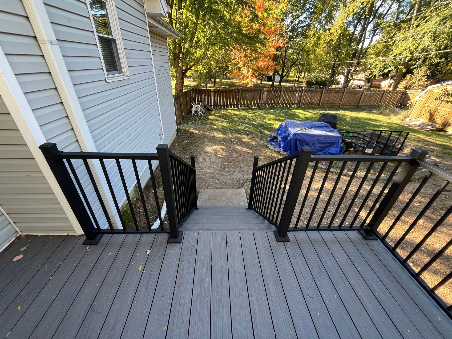 Deck with dark railings and steps leading to a yard with a fence and fall foliage.
