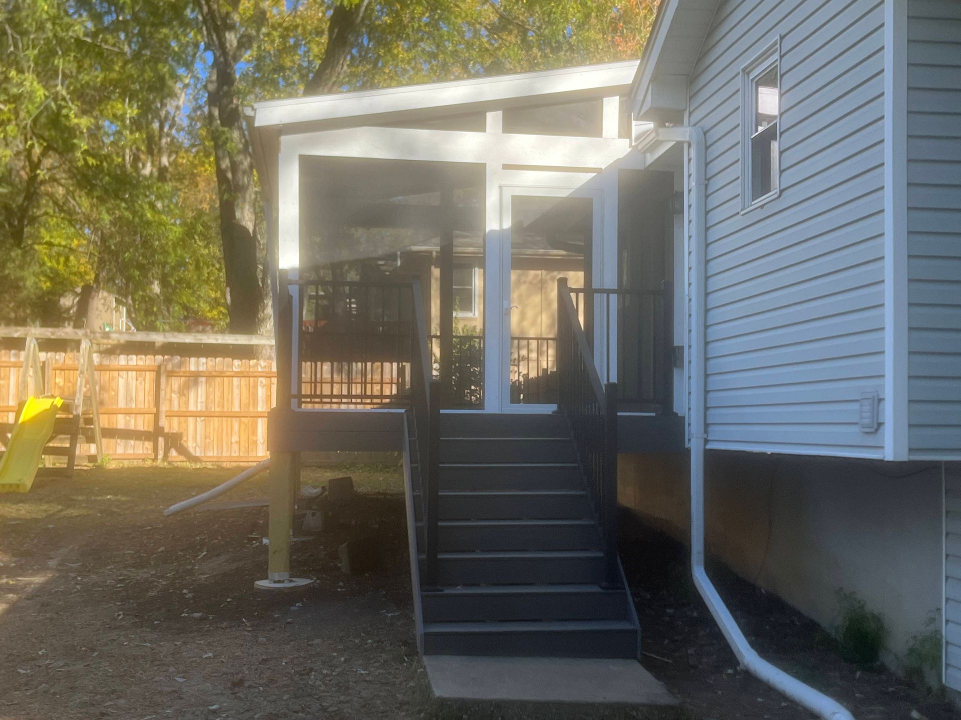 Backyard deck with gray stairs, black railing, and white-painted overhead cover, attached to a light-colored house.