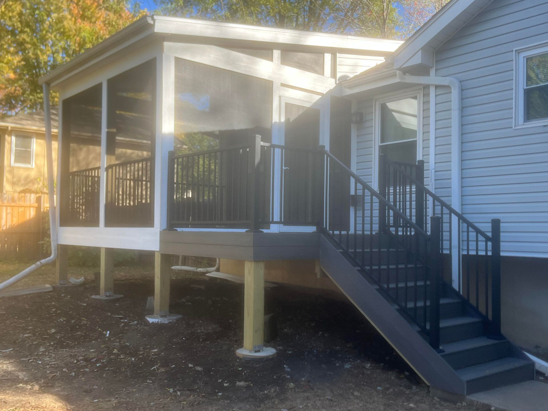 A screened-in porch with stairs attached to a light blue house. Dark gray railings.