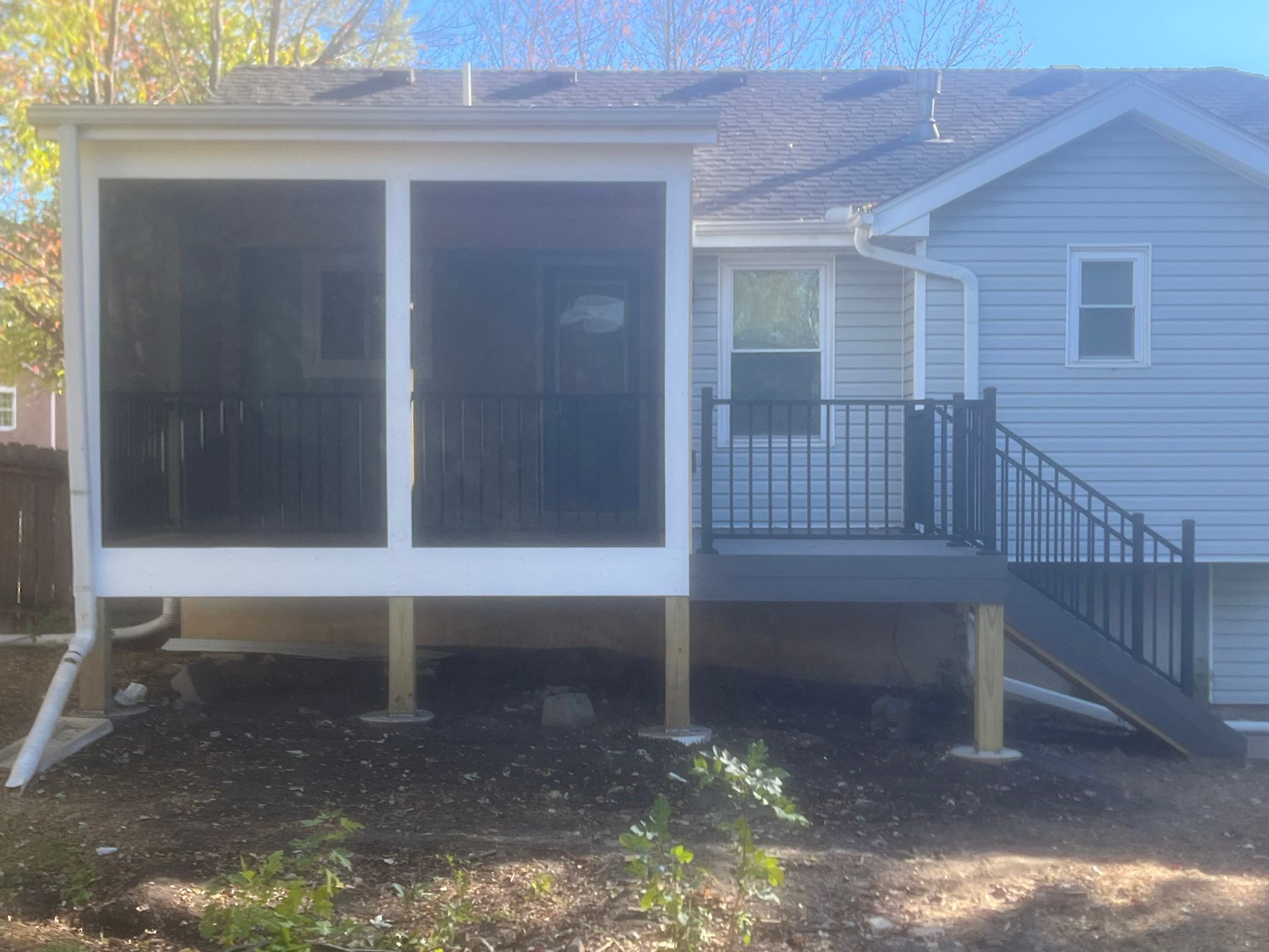 Screened-in porch and deck attached to a light blue house. Dark gray screening, black railing, and wooden support beams.