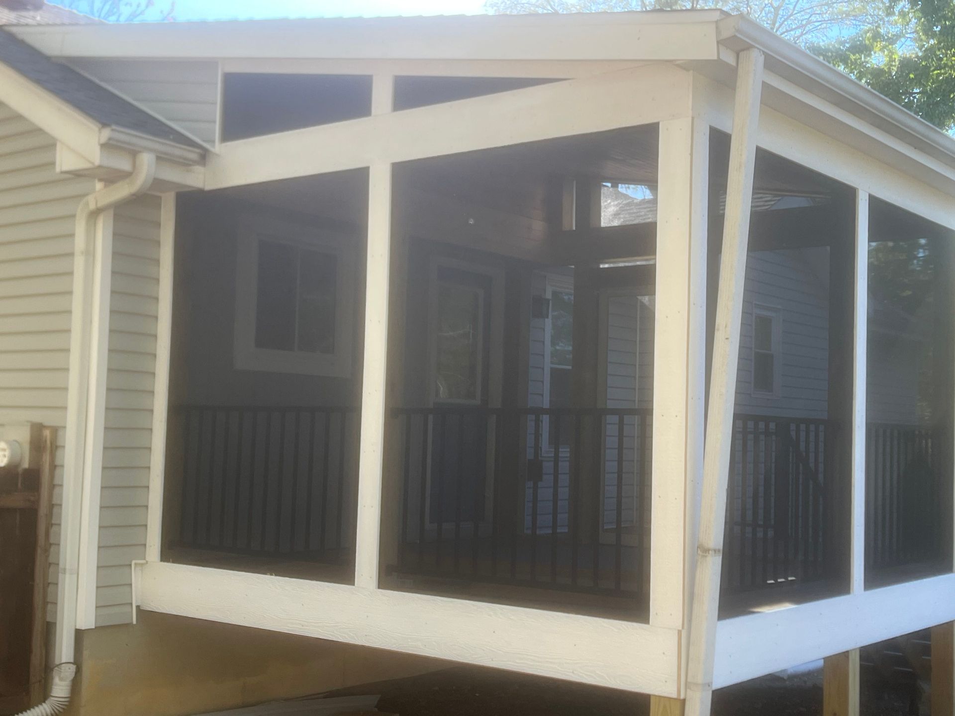 Screened porch with white frame, black railings, and screen walls attached to a house.